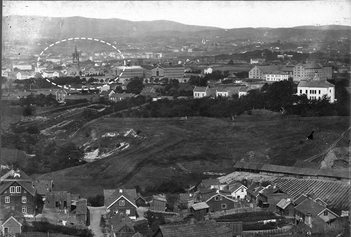 BYGÅRDER: Grønland kirke og skolebygningen (skribentens markering) sett fra Ekebergskrenten rundt 1870–1880. Bildet viser at det, tross en rekke nybygg, fremdeles var korte strekninger mellom by og land. Det vil si: Området øst for Grønland, inkludert Ekeberg, ble også del av byen som følge av utvidelsen i 1878 – altså i tida dette bildet ble tatt.